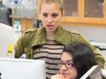 Two students talk while looking at a desktop computer in lab