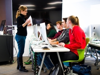 Prof. Peck talks to four students that each use a desktop computer