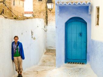 Student stands against white painted outdoor wall near a bright blue door in the streets of Morocco