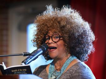 NC Poet Laureate, Jaki Shelton Green stands at podium holding her book, and reading poems into the microphone
