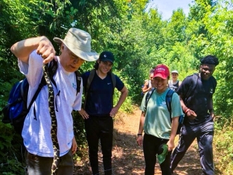 Guide holds a wild snake with his hands while group of sustainability scholars watch