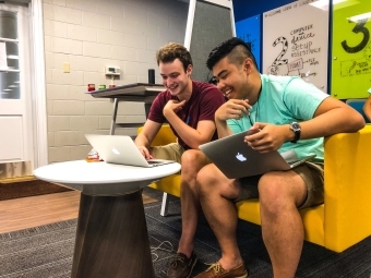 Two students sit together at the Technology & Innovation office having their computers fixed