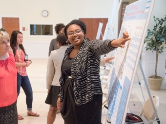 Student presents data project at a poster symposium pointing to her poster while audience listens