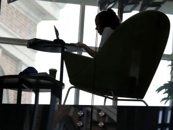 Student studies in the Wall Center sitting in an oversized chair by the window