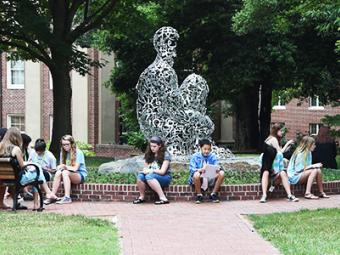 Students in a summer program on campus gathered around a campus sculpture