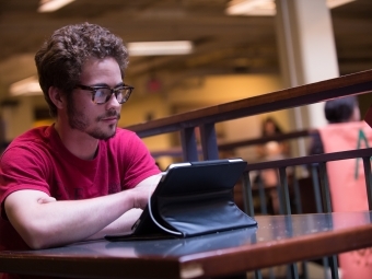 Student sits at Davis Cafe and looks at a tablet