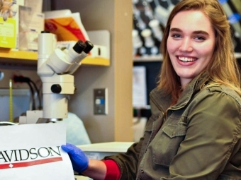 Student in lab at summer internship holds up a sign with the Davidson logo