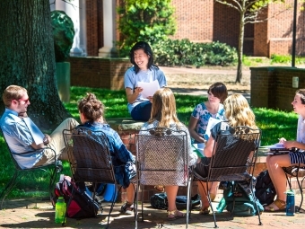 Student group sits on outdoor furniture by grassy area
