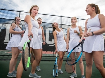 Women's Tennis team is on the court with rackets hanging out and laughing