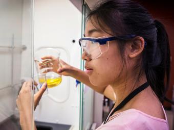 Student in lab holds a beaker of yellow liquid