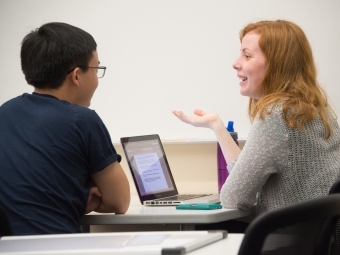 Student tutors another student while both sit at table and look at laptop