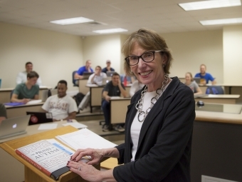 Prof. Roberts smiles at camera while leading class from podium
