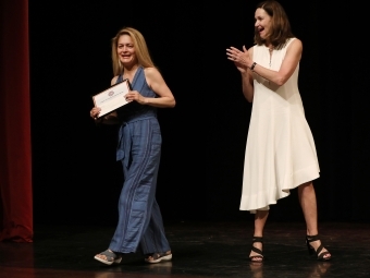 Irsa Vargas with plaque as Carol Quillen cheers her on stage