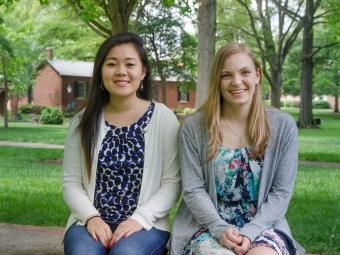 Two students sit outside next to one another on bench