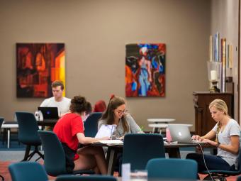 Students gather in the library and study with colorful art behind them