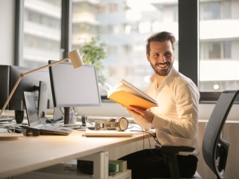 Man at computer holding a book while at work