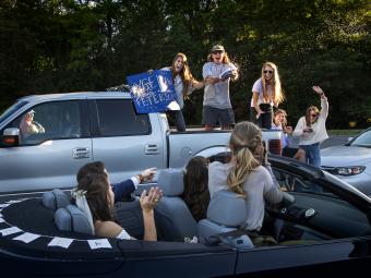 Friends in trunk of truck cheering with sign 