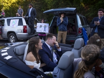 Caroline and Tyler smiling at guests in front of cars cheering