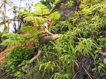 Lydia climbs hillside with vegetation and magenta orchids