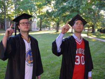 two graduates in basketball jerseys pointing to the sky
