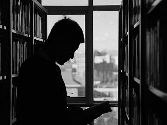 Silhouette of man in library reading a book