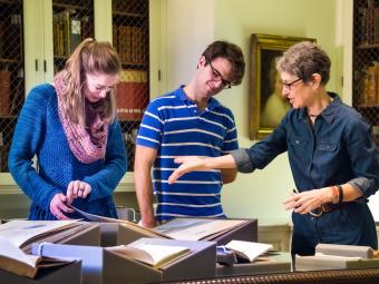 Sharon Byrd talks to two students as they all examine rare books