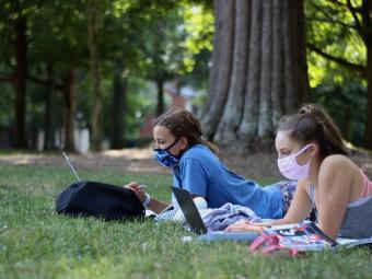 Two students with masks on the lawn on computers