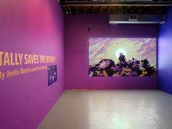 Tally Saves the Internet Exhibit text on wall in purple room, with screen projecting creature on pile of rubble