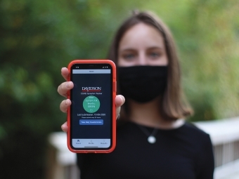 Student Holds Up Green Covid Symptom Tracker on her phone while wearing Mask