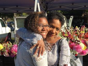 Maia Harrell '20 and Janet Stoval '85 hug by flowers