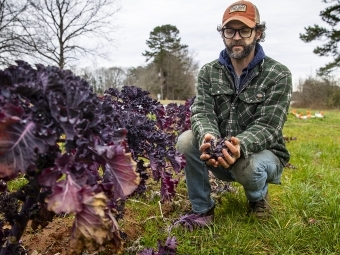 Joe Rowland kneels with Produce at Davidson College Farm