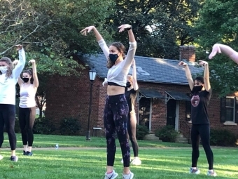 students with masks dancing on campus lawn