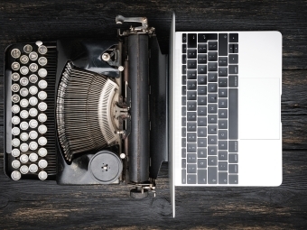 Antique typewriter next to modern laptop on wooden table