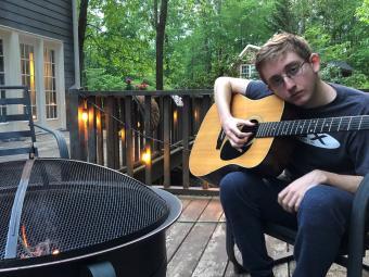 Davidson College music scholarship student Cooper Ray Oljeski '25 holds guitar on patio with firepit