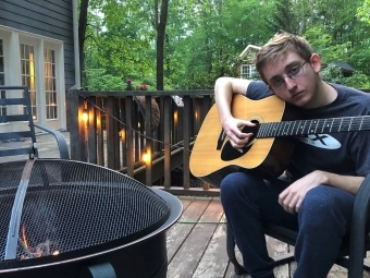 Davidson College music scholarship student Cooper Ray Oljeski '25 holds guitar on patio with firepit