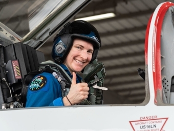 Astronaut Kayla Barron does Thumbs Up while in uniform inside space craft