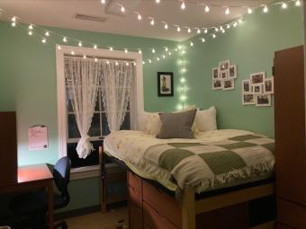 Green room with bed, armoire and desk, twinkle lights, curtains, picture frames, and bedding