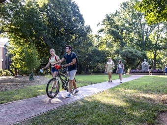 Two students walking, one holding a bike and talking on campus