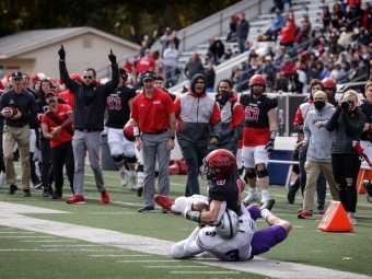 Tackle in the Foreground of Field with Coaches in Background