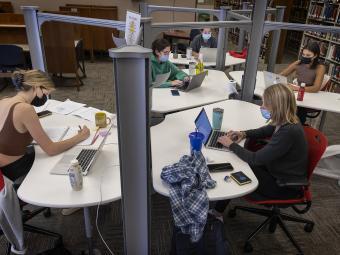 Group of students studying at pod of desks in library for final exams