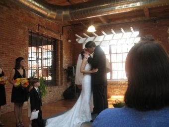 Andrea and David share a kiss at their wedding with guests standing around