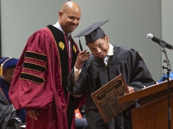 Brandon Reid in cap and gown holding award in front of podium with Dean Byron McCrae