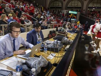 Sam Goldfarb on his laptop with a headset on at a basketball game at Davidson