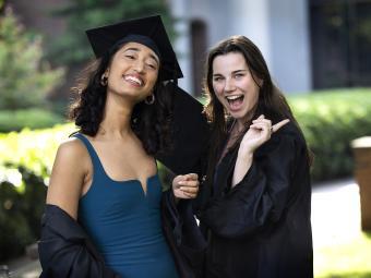 two graduates in cap and gown pose smiling