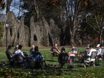 students sitting in circle of chairs outside on the campus lawn