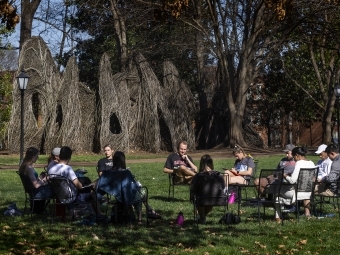 students sitting in circle of chairs outside on the campus lawn 