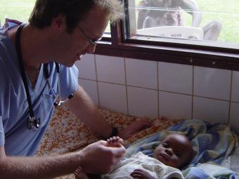 Photo of Benjamin Gilmer examining an infant in Gabon