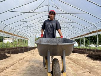 Student in greenhouse with wheelbarrow