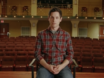 Person sitting in chair onstage. Behind them is an empty auditorium