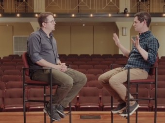 Two men facing each other in chairs onstage